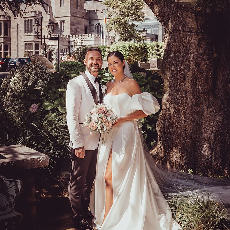 A bridge and groom stand in the garden at Clontarf Castle Wedding Venue in Dublin.